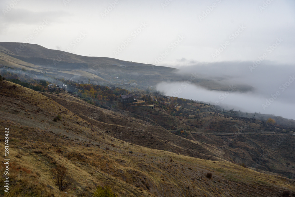 Mountains shrouded in mist in the season of golden autumn on a cloudy day, view of the ancient village in the gorge from the top of the mountain.