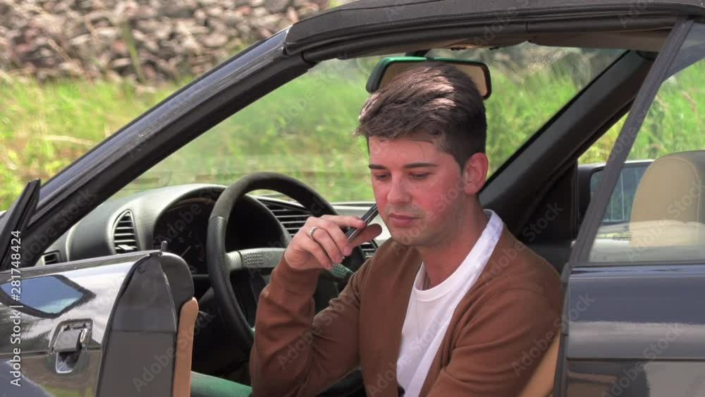 A young man sits in a broken car and makes phone calls A young man sits in a broken car and makes phone calls