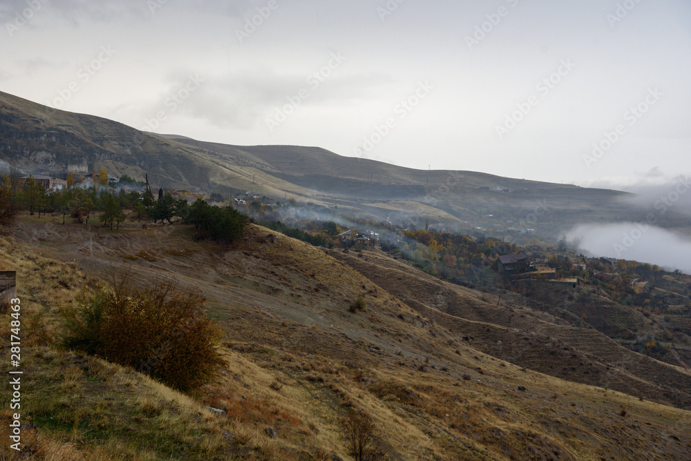 Mountains shrouded in mist in the season of golden autumn on a cloudy day, view of the ancient village in the gorge from the top of the mountain.