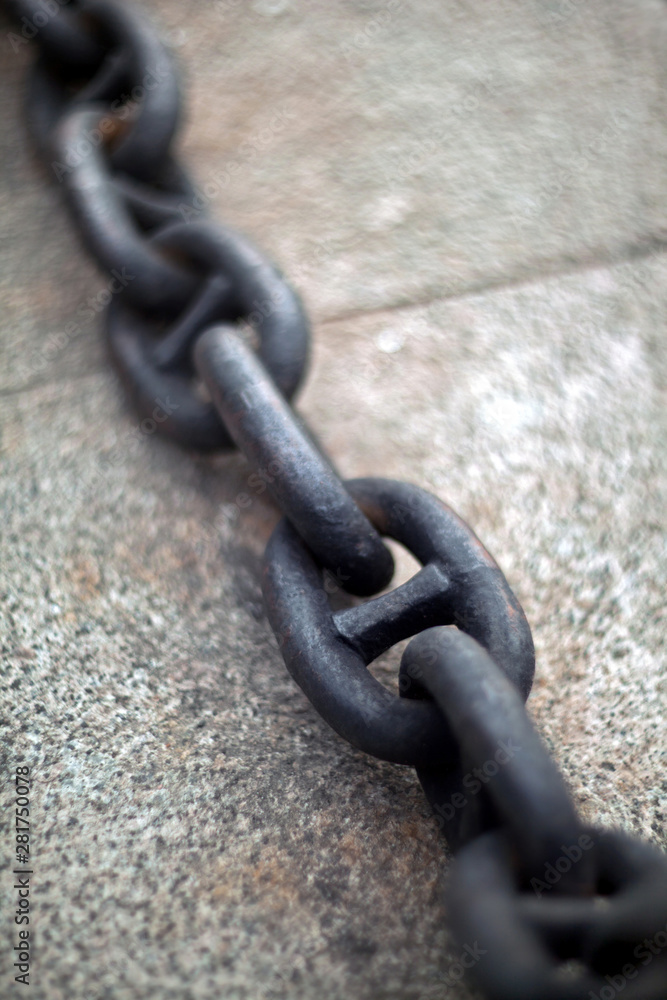 An old heavy iron chain from a sea anchor lying on a pier concrete slab with blurred background. An old heavy iron chain from a sea anchor lying on a pier concrete slab with blurred background.