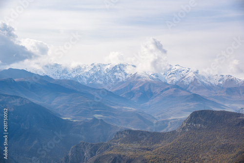 view of the mountain ranges on a bright sunny day with clouds in the sky and sun rays passing through the clouds, snow-covered tops of the mountain slopes on the horizon.