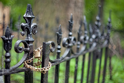 Metal top of art casting on a grave fence in the shape of a bourbon lily with golden chain and lock and a blurred background.