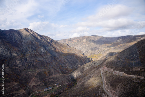 view of the mountain road on a bright sunny day with clouds in the sky, mountain ranges painted in senny yellow-golden brown.