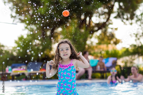 happy little girl with her hair down in a bright swimsuit playing ball in the pool on a Sunny summer day
