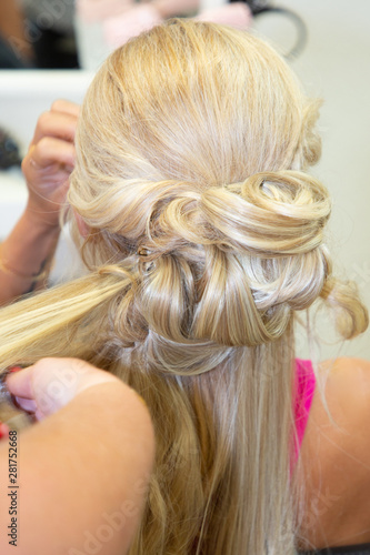 woman hairdresser making hairstyle to blonde girl bride in beauty salon