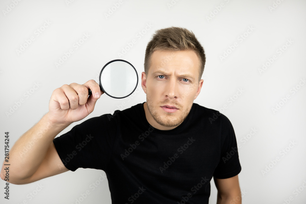 handsome young man wearing black t-shirt holding magnifying glass near his eye looks suspicious isolated white background handsome young man wearing black t-shirt holding magnifying glass near his eye looks suspicious isolated white background