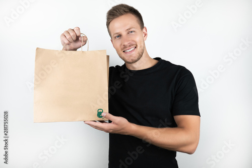 handsome young man wearing black t-shirt holding shopping craft papper bag with goods on isolated white background