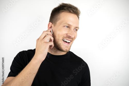 handsome young smiling man wearing black t-shirt having pleasant phone conversation using wireless headphones on isolated white background