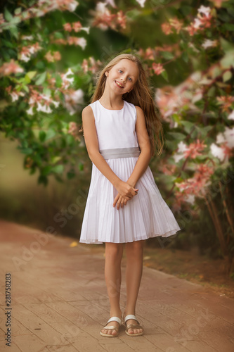 Girl portrait standing in beautiful white dress outside in park or garden near flowers bush.
