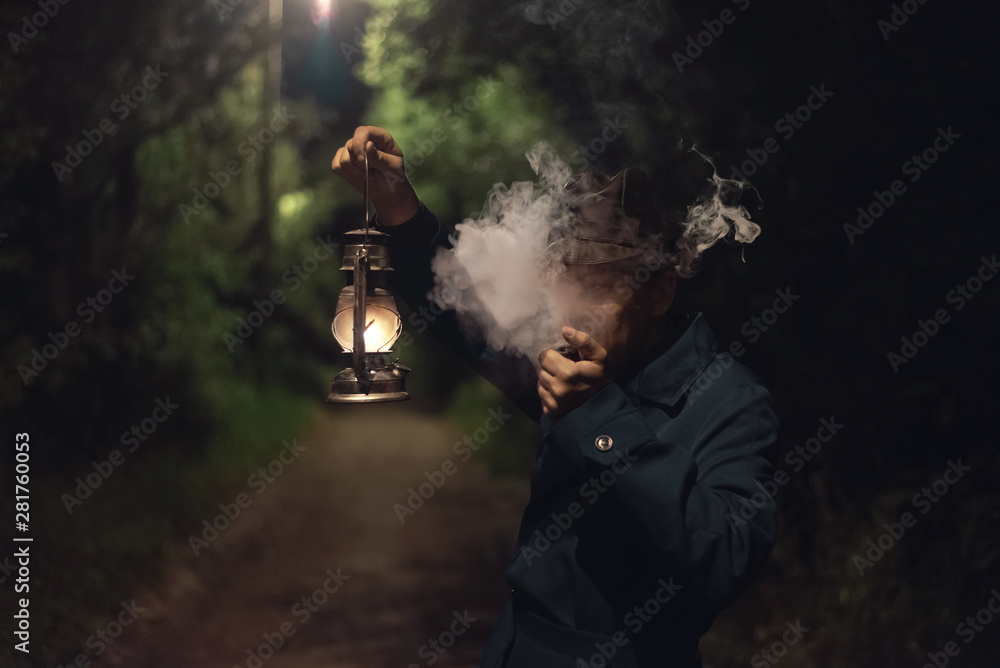 Detective agent in a hat and coat is holding in hand a kerosene lamp and smokes his smoking pipe. Detective agent in a hat and coat is holding in hand a kerosene lamp and smokes his smoking pipe.