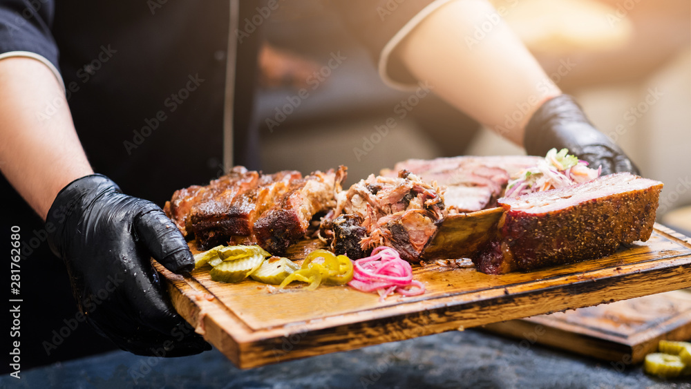 Professional catering. Cropped shot of chef holding wooden board with smoked meat assortment. - obrazy, fototapety, plakaty 