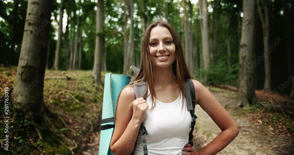 Pretty female hiker with backpack standing on forest road and smiling, portrait of tourist Pretty female hiker with backpack standing on forest road and smiling, portrait of tourist