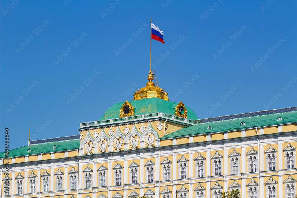 Obraz premium Wielki Kreml Palace z macha flagą Federacji Rosyjskiej na dachu na tle błękitnego nieba w słoneczny poranek