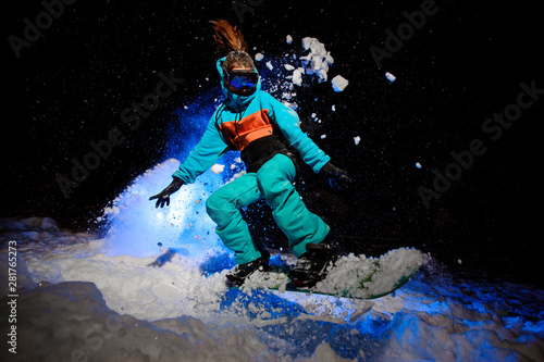 Female snowboarder dressed in a orange and blue sportswear jumping on the snow © fesenko