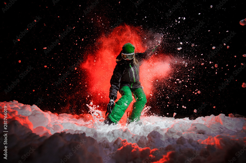 Female snowboarder dressed in a green sportswear standing on the snow slope