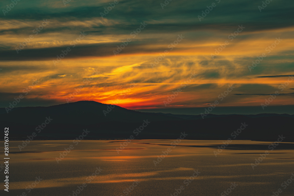 Beautiful burning cloudy sunset at the lake with sun gone behind the mountains Beautiful burning cloudy sunset at the lake with sun gone behind the mountains