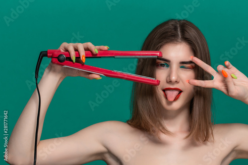 Portrait of beautiful young woman with bright color make-up doing hair style herself with a purple straightening iron.