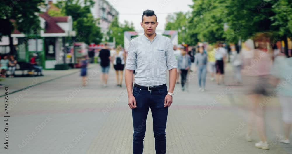 Zoom out time lapse of attractive mixed race guy standing in city street among crowd of people rushing around on summer day. People and society concept. Zoom out time lapse of attractive mixed race guy standing in city street among crowd of people rushing around on summer day. People and society concept.
