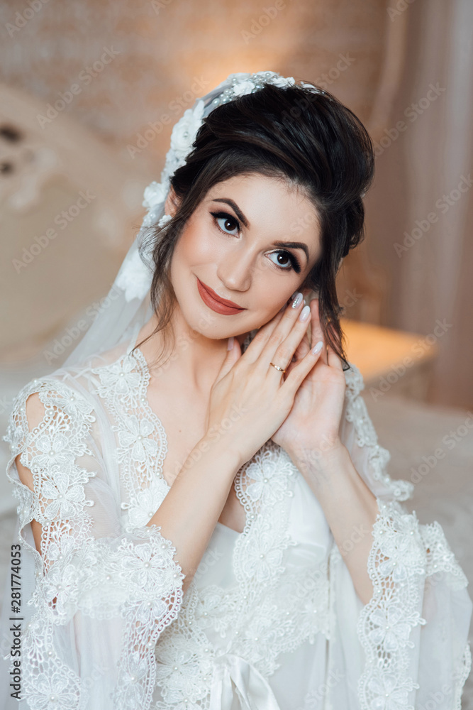 Close-up portrait of a brown-eyed girl with dark hair and hands near the face. Bride with beautiful makeup. Morning of beautiful bride. Bride's fees. Elegant hairstyle and makeup.
