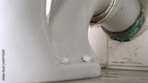 Leaking water from a toilet due to pipe blockage or worn out parts. Smelly water drops dropping behind the toilet from dirty pipe. Toilet leakage, bad smell, plumber needs to take care of it