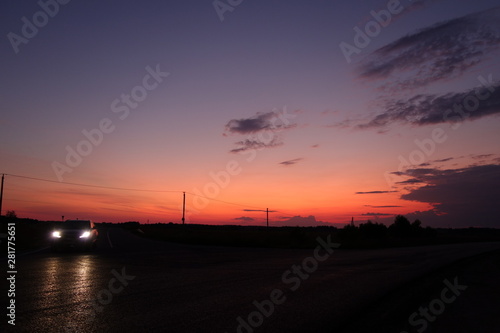 Sunset noir in red and orange with car headlights reflected on tarmac in black foreground