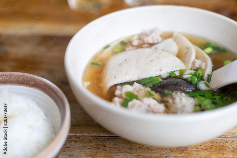 Soup with pock, pock stick, mushroom, vegetable in white bowl near have rice in small bowl on wood table. with copy space for text or design