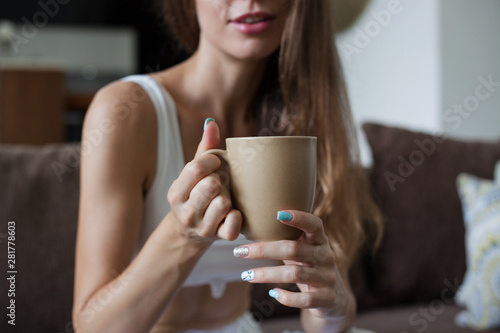 Female hands holding broun cup of tea, color manicure, girl is dressed in white clothes. horizontal frame