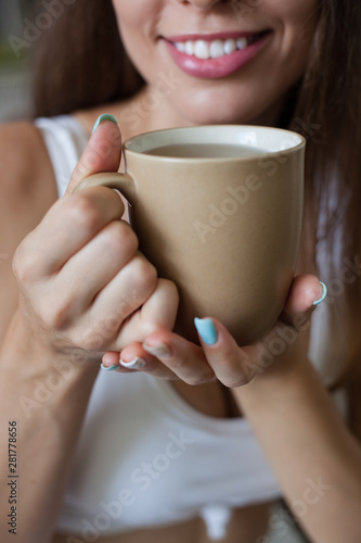 Female hands holding broun cup of tea, color manicure, smiling girl is dressed in white clothes. vertical frame