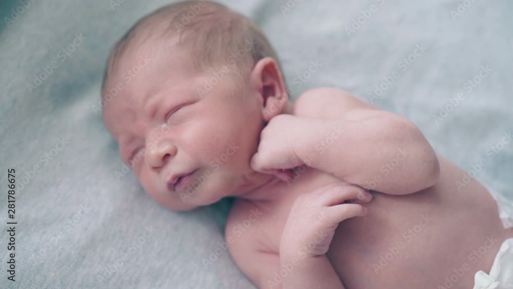 restless and crying newborn boy with fair hair lies on baby changing table and calms down extreme close view restless and crying newborn boy with fair hair lies on baby changing table and calms down extreme close view