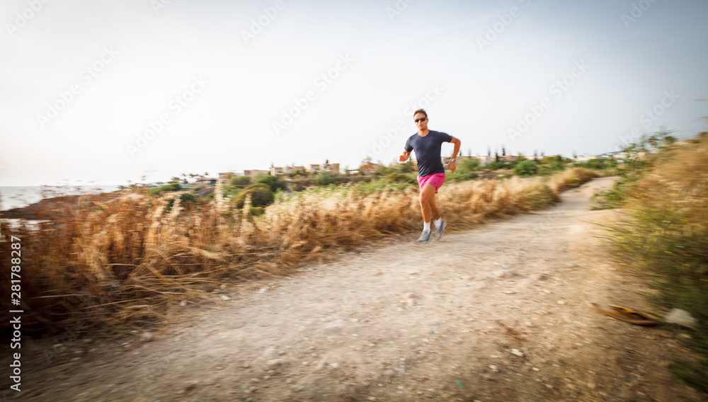 Fototapeta premium Caucasian young man running on a seacost path on a lovely summer evening, training for marathon (motion blurred image).