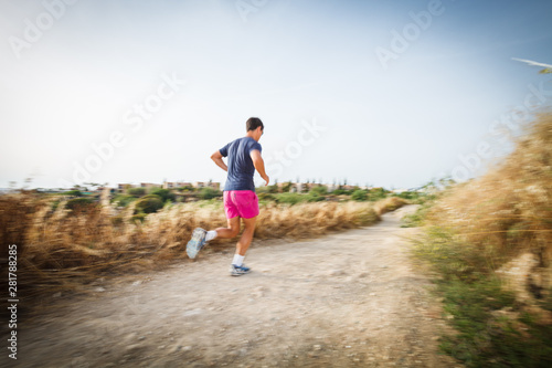 Caucasian young man running on a seacost path on a lovely summer evening, training for marathon (motion blurred image).