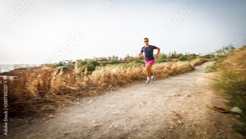 Caucasian young man running on a seacost path on a lovely summer evening, training for marathon (motion blurred image).