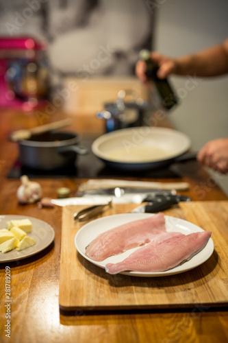 rohe Fisch Filets auf Teller in der Küche, dahinter unscharf Herd, Pfanne, Hände eines Mannes, Ölflasche