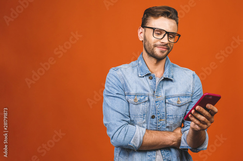 Great news! Happy young man in glasses typing sms isolated against orange background. © denis_vermenko