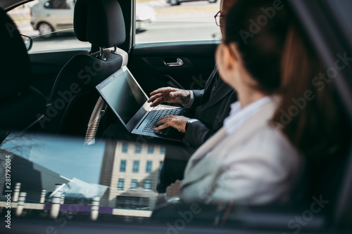 Good looking senior business man and woman coworker sitting on backseat in luxury car. They talking  smiling and using laptop and smart phones. Transportation in corporate business concept.