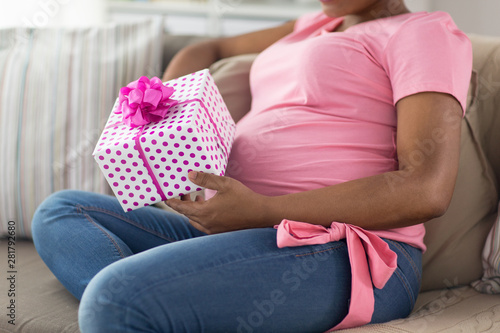 pregnancy, holidays and people concept - close up of pregnant african american woman sitting on sofa with gift box at home
