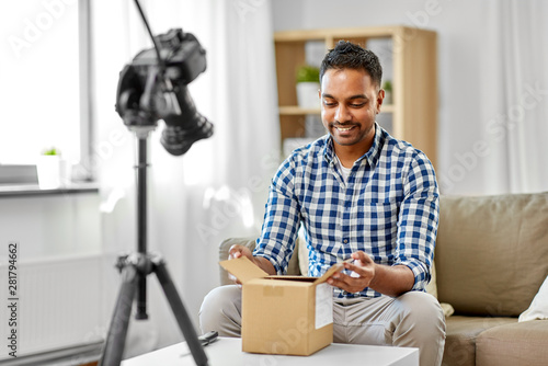 mail delivery, shipment and blogging concept - happy indian male blogger opening parcel box and recording unboxing video with camera at home photo