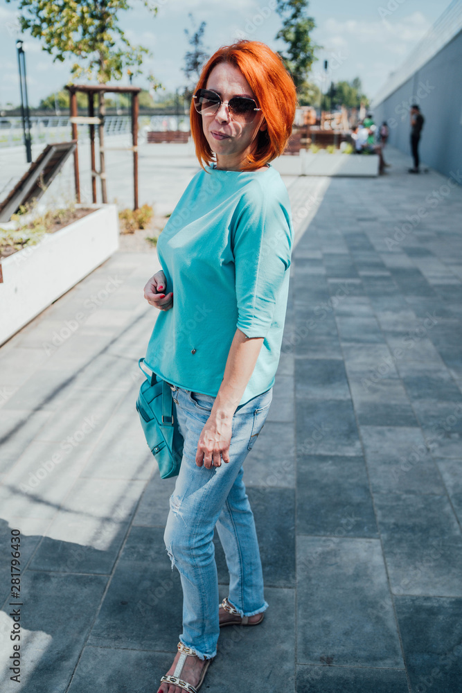 Fototapeta premium Portrait of young red-haired woman in casual clothes and with sunglasses.