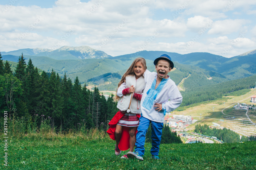 Brother and sister in national clothes in the mountains. Children travel. Beautiful boy and beautiful girl smiling in nature