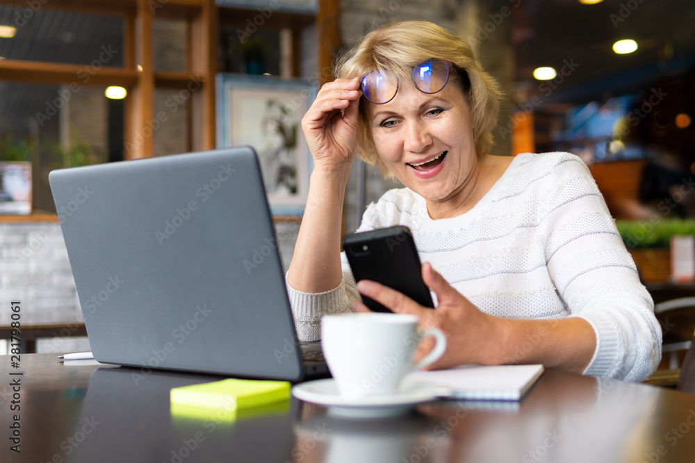 A middle-aged woman with a laptop works in a cafe in the office, she is a freelancer. A woman with glasses sits at a table with a Cup of herbal tea. She is talking on the phone. A middle-aged woman with a laptop works in a cafe in the office, she is a freelancer. A woman with glasses sits at a table with a Cup of herbal tea. She is talking on the phone.