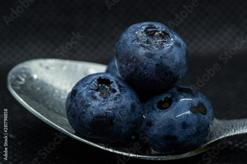 Blueberries Macro closeup photo of superimposed on top of each other and tiled in a teaspoon on a dark background glistening in drops of fresh water.