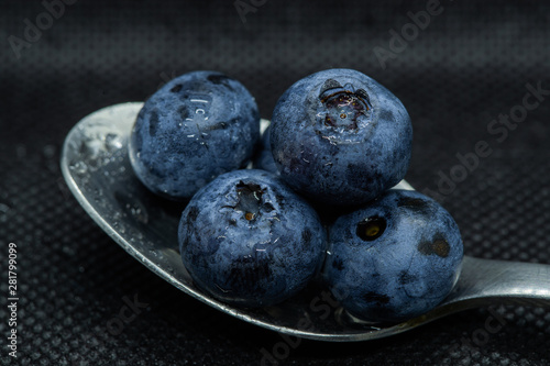 Blueberries Macro closeup photo of superimposed on top of each other and tiled in a teaspoon on a dark background glistening in drops of fresh water.