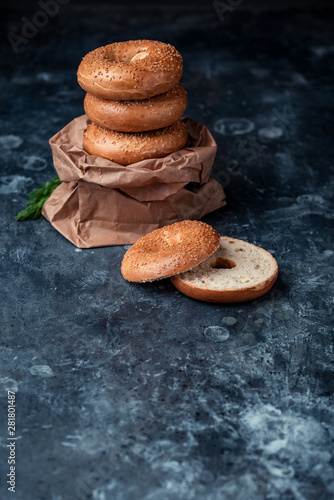 Stacked Bagels partly in a paper bag on a dark, atmospheric surface with a cut bagel in front