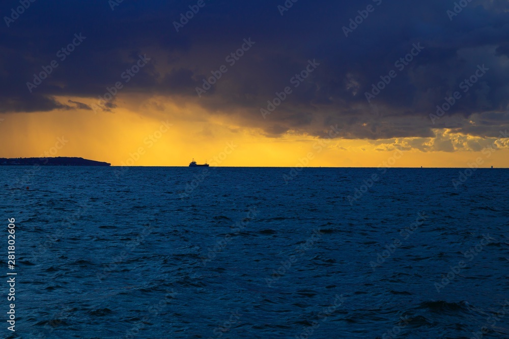 Fototapeta premium Dramatic sunset through a cloudy dark sky over the ocean.