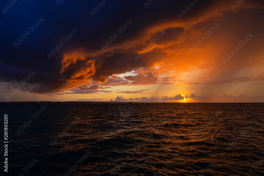Obraz premium Dramatic sunset through a cloudy dark sky over the ocean.