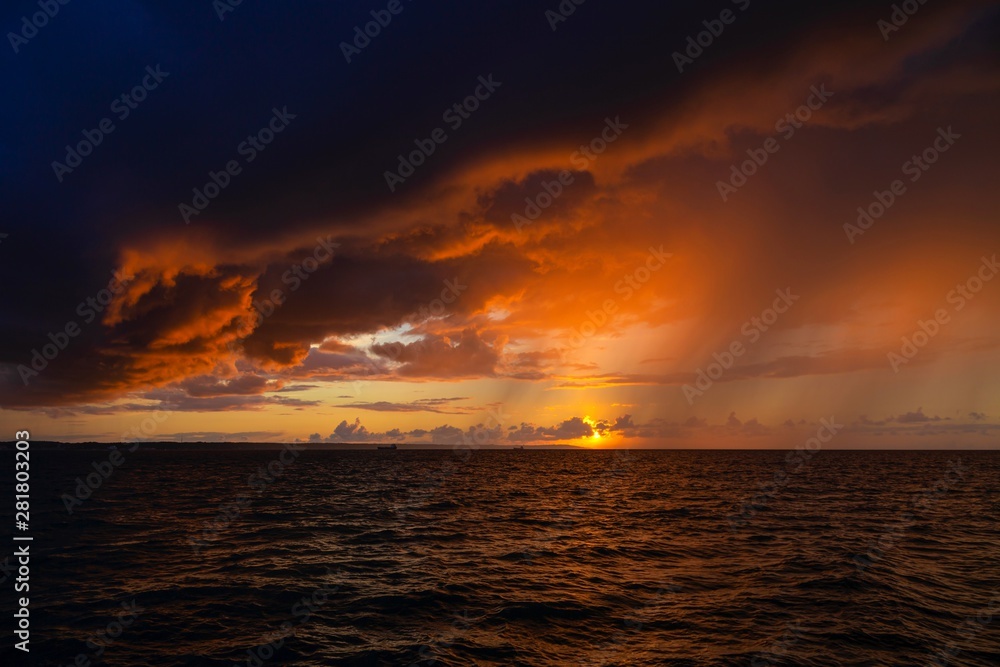 Obraz premium Dramatic sunset through a cloudy dark sky over the ocean.