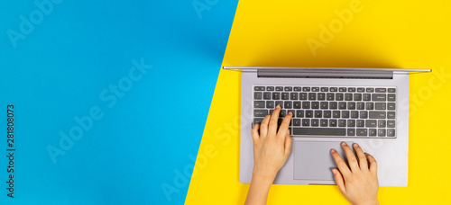Kid hands typing on laptop computer keyboard, top view, yellow and blue background