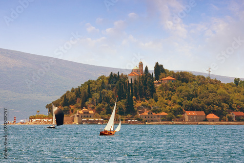 Picturesque Mediterranean landscape with sailboats on the water, sunny vacations. Montenegro, Adriatic Sea, Bay of Kotor, view of Kamenari village with Church of Sveta Nedjelja