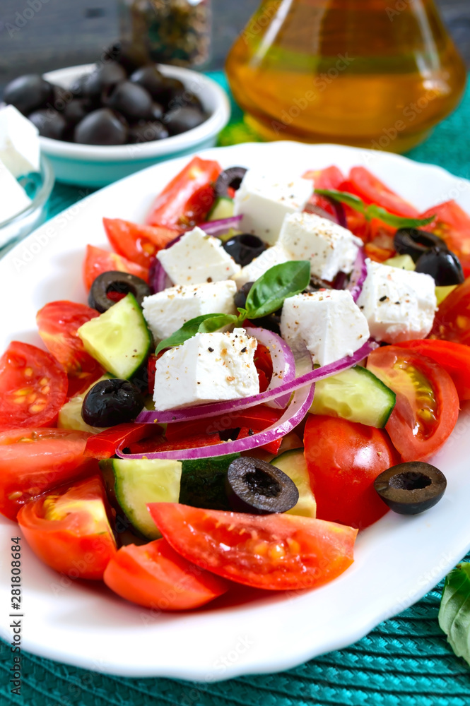 Tasty  vitamin salad with fresh vegetables, feta, black olives, basil sauce on a white plate on a wooden background.