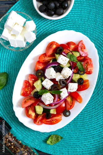 Tasty  vitamin salad with fresh vegetables, feta, black olives, basil sauce on a white plate on a wooden background. Top view.